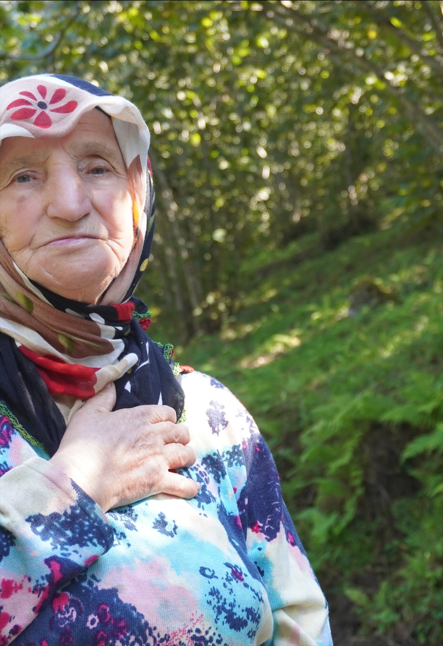 Bäuerin mit der Hand auf dem Herzen zwischen Haselnusssträuchern