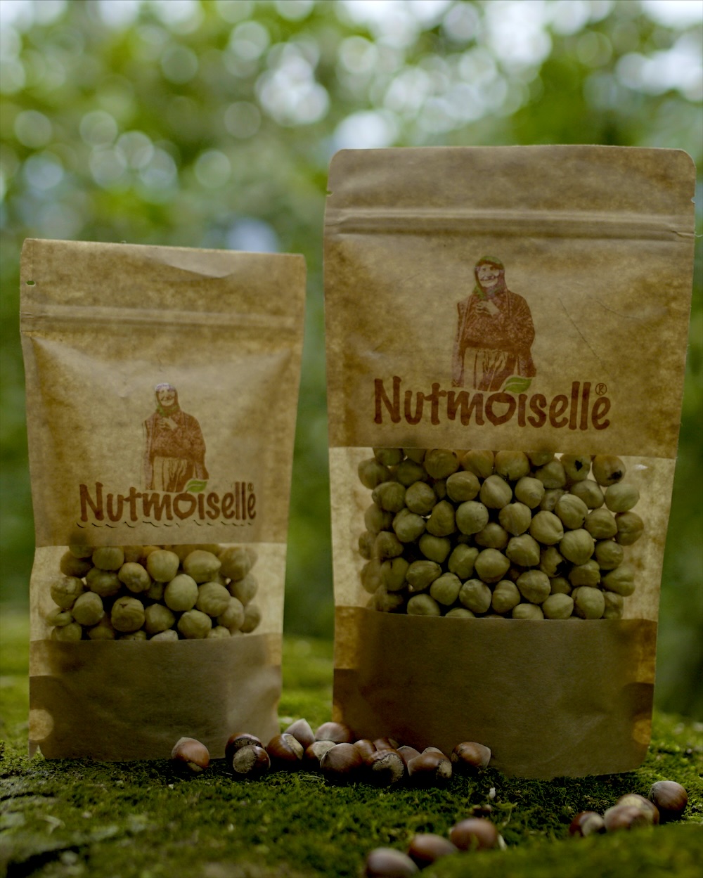 Zwei Nutmoiselle-Beutel mit Haselnusskernen auf einem bemoosten Stein im Wald
